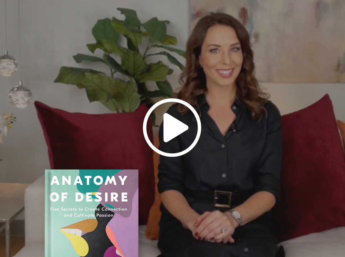Woman sitting on a couch with a book titled 'Anatomy of Desire' next to her.